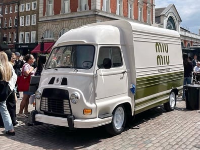 The Miu Miu Renault Estafette hire, in white, on the roadside around people.