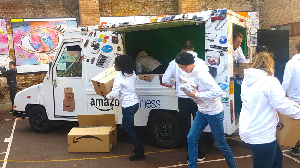 Amazon's white US postal van in a school gym, with staff delivering boxes.