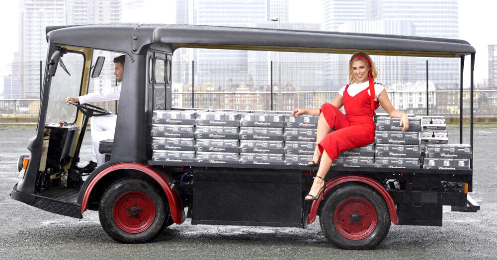 A woman in red poses with the Budweiser electric milk float, parked near Canary Wharf in London.