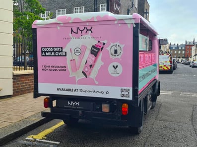 NYX electric milk float hire, viewed from behind with info about the cosmetics products.