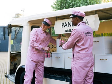 Two men in pink dressed as milkmen pose next to Pandora's electric milk float.