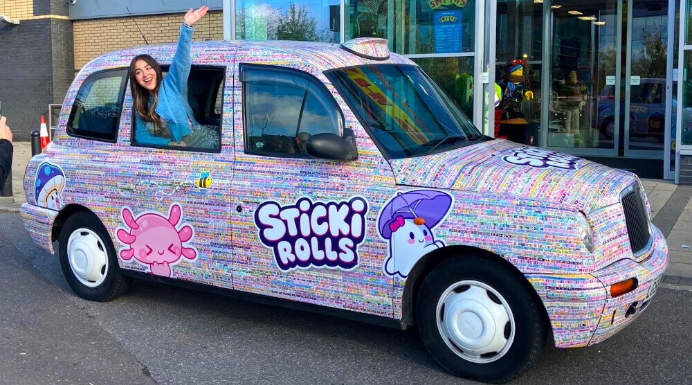 The Sticki Rolls fully wrapped and branded taxi hire, with a young woman inside and smiling for the camera.